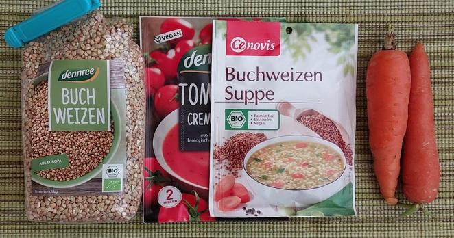 Die Hauptzutaten zur Suppe auf dem moosgrün-gestreiften Platzdeckchen:
- dennree Buchweizen (Marke aber egal)
- dennree Tomatencreme-Suppe, vegan (Marke egal, es geht alternativ auch Gemüsesuppe), halb verdeckt, weil nur 1/2 Tüte verwendet
- Cenovis Buchweizensuppe (kenne keine andere Marke)
- 2 mittelkleine Karotten