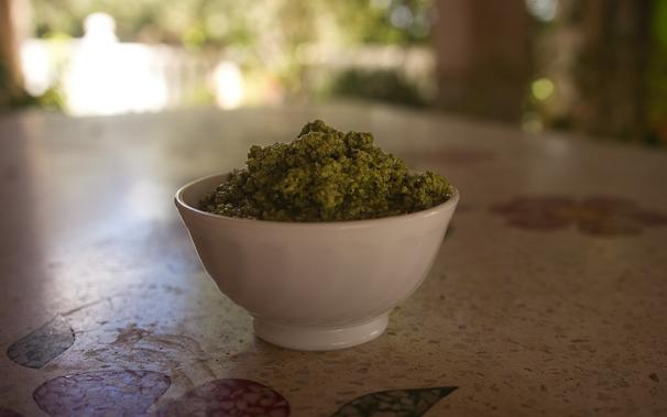 A bowl filled with finished broad bean pesto is placed on a stone table in the garden.