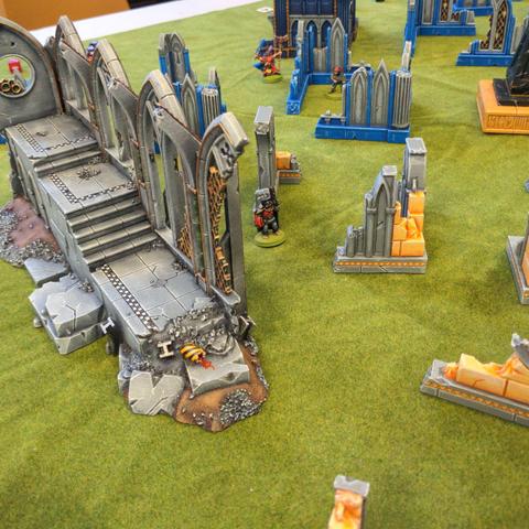 A vibrantly coloured scifi battle field, covered in blue and yellow ruins and a large grey and gold ruined cathedral.
