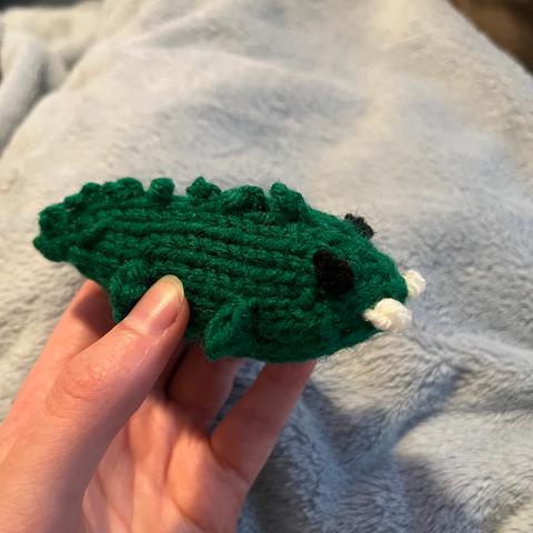 A cute little knitted alligator, very round, with two big front teeth made of yarn