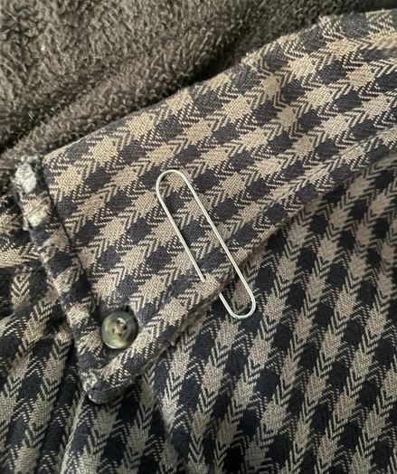 Photo of a grey and black plaid shirt with button down collar and attached paperclip.