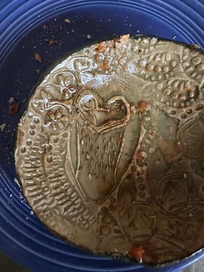 owl design stamped on a small ceramic bowl with a dark blue vintage fiesta plate behind it. all dishes are dirty with bits of breakfast