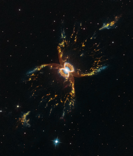 Image of The Southern Crab Nebula captured by the Hubble Space Telescope. This planetary nebula is comprised of a  symmetrical, butterfly-like structure with bright, glowing filaments of gas and dust expanding outward from a central white ring. The nebula appears to have four main lobes, glowing in shades of gold, blue, and orange, set against a black background. Distant stars are scattered throughout the image.