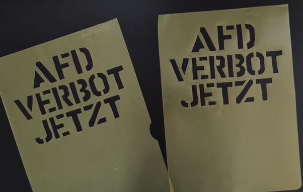 Zwei Plastikfolien mit ausgeschnittenem Slogan
"AFD VERBOT JETZT"