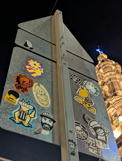 stickers on a street sign on the foreground and a cathedral on the background