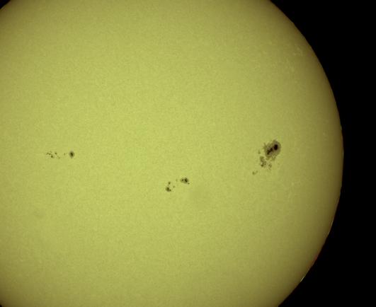 A close-up image of the Sun showing several dark sunspots scattered across its bright yellow surface.