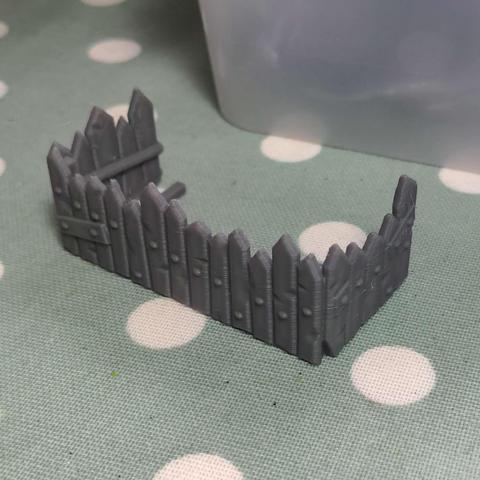 A grey plastic model of a poorly made picket fence sitting on a mint green and white polkadot tablecloth.
