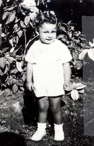 A young boy standing in front of a tree. He has short trousers and a short-sleeve blouse.