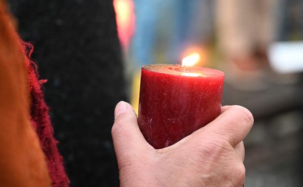 Eine Hand hält eine brennende rote Stumpenkerze