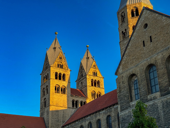 Eine von der Morgensonne angestrahlte Kirche (Liebfrauenkirche Halberstadt) vor tiefblauem Himmel, dazwischen rote Ziegeldächer