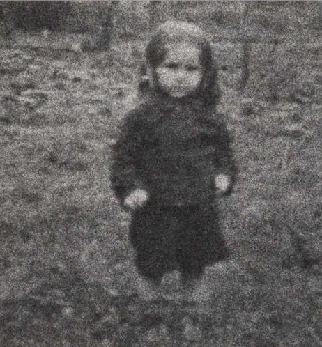 A blurry photo of a little girl standing on the grass.