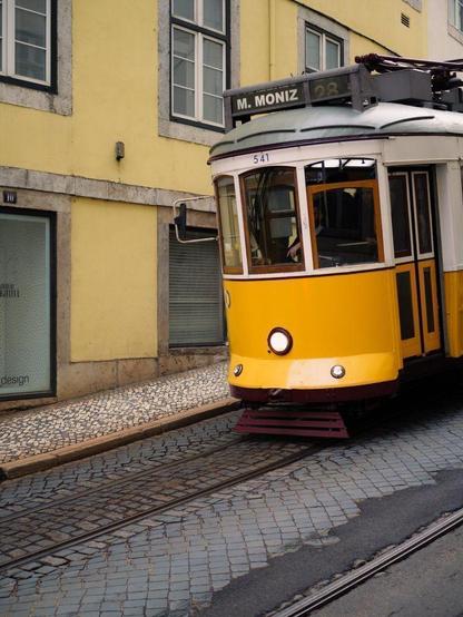 A Lisbon's yellow tram riding down a sloping street.