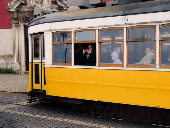 A yellow tram in Lisbon with a young woman taking a photograph through an open window.