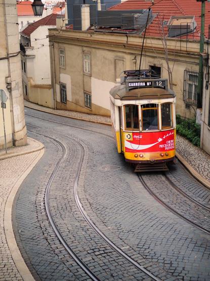 A yellow tram riding down a sloping street.