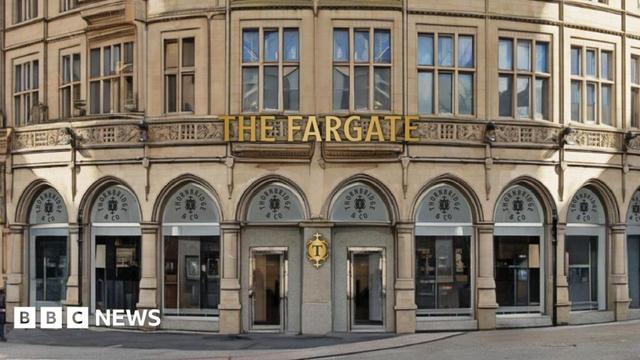 An old stone-build building with many curved archways at ground level. In columns above them are many windows. Gold lettering saying "The Fargate" is at the front of the building above the entrance.