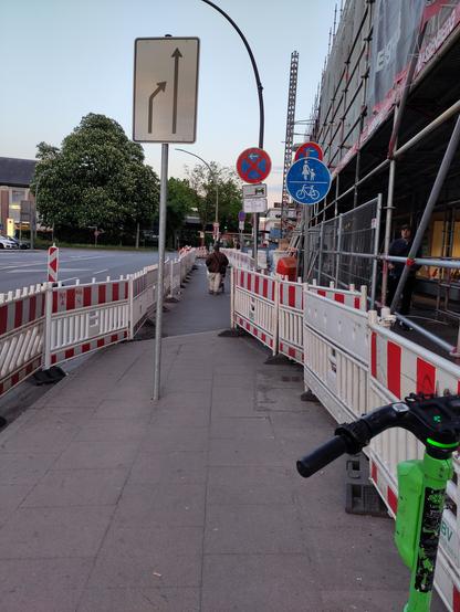 Der auf die Fahrbahn verlegte gemeinsame Geh- und Radweg ist an einer Stelle kaum breiter als einen Meter, beim Belagwechsel ist eine Stufe zu überwinden, ein Schild steht mitten im Weg und im Vordergrund parkt auch noch ein E-Roller. Kfz-Verkehr wird nicht sichtbar eingeschränkt. Leider ist gerade keinen Lastenrad fürs Foto vorbei gekommen 🥹