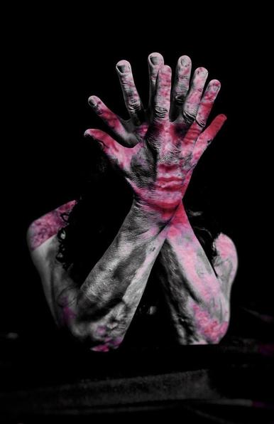Black-and-white photo, double exposure with a photo in red tones. Portrait format, self-portrait. A person, elbows resting on an unrecognizable black desk, hands with fingers fanned out, head lowered behind the arms so that only dark hair is visible. The arms appear strangely grained due to the light application of paint, as if coated with ash. Additionally exposed, the shadowy face of a stone sculpture in red tones, visible in the area of ​​the hands. Overall impression: introverted, but with the face slightly glowing from within, like a double person: inside and out, reason and emotion.