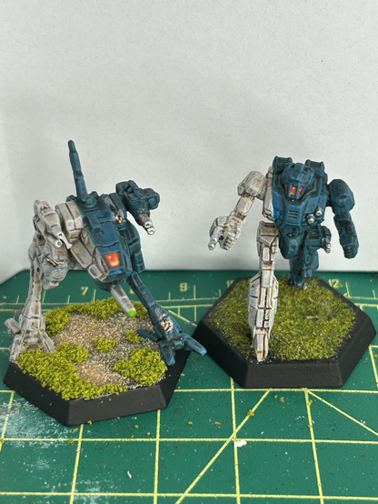 Two partially blue, partially white Battle Tag robots that Remind me of a Shark and a T-rex