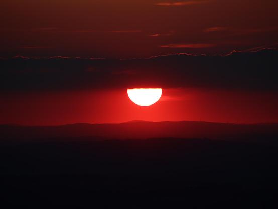 die sonne duckt dich unter ein wolkenband und scheint rot auf die schattigen hügel