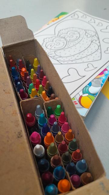 An open box of crayons with a coloring book to the side