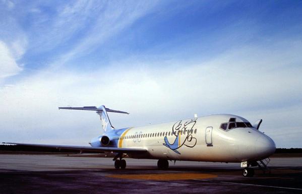 Plane is seen parked somewhere remote. The sky is blue with long wispy clouds.