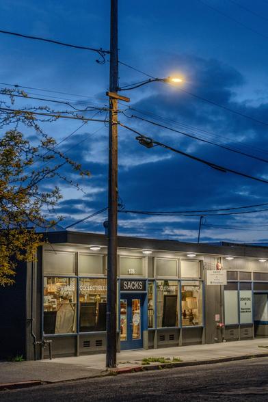 A photograph showing the striking color difference between the rising sun, a lone streetlamp, and the mildly-illuminated storefront of Sacks.