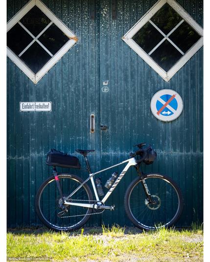 A Canyon Exceed with drop bars and Tailfin bikepacking packs front (Drop Bar Bag Small) and rear (Aeropack Cargo) in front of an old barn door.