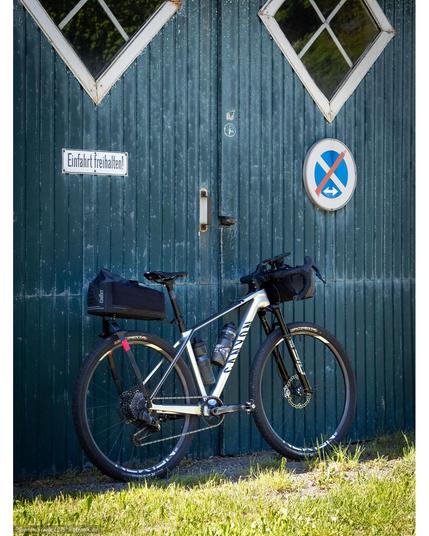 A Canyon Exceed with drop bars and Tailfin bikepacking packs front (Drop Bar Bag Small) and rear (Aeropack Cargo) in front of an old barn door.