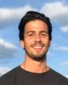 Michael Charlebois' headshot. He has short black hair and is wearing a black shirt. Behind him is the sky with clouds.