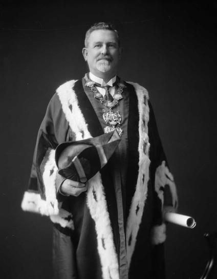 Black-and-white portrait photo: Charles John Boyd Norwood in mayoral attire. 1925–1927. Description: A three-quarters portrait of a short-haired man with a goatee beard and moustache. His hair and moustache are greying, his beard largely white. He holds a scroll in his left hand and the mayoral hat in his right hand. Citation: S P Andrew Ltd: Portrait negatives. Ref: 1/1-018682-F. Alexander Turnbull Library, Wellington, New Zealand. https://natlib.govt.nz/records/23214990