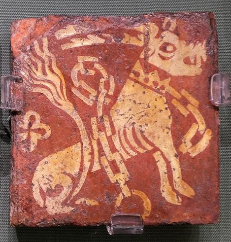 A reddish tile with a cream coloured design of a beast with long horns and pig-like head and a dog-like body. It is chained around the neck.