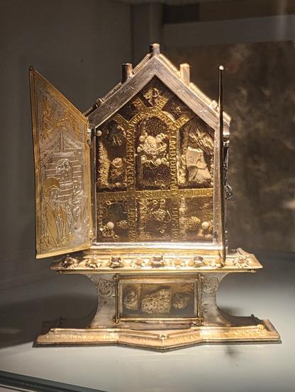 small silver “cabinet” reliquary in the shape of a triptych altarpiece, the doors open to reveal hagiographical scenes engraved on the inside of the doors and about a dozen pieces of bone displayed under glass in the central piece.