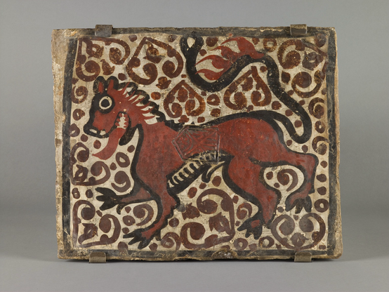 “Overlaying the lively animal decorating the surface, this tile bears the stamp of the kilns at Paterna, just outside Valencia, Spain. It would have decorated a ceiling inside a local building, suspended between wooden rafters. The term for such ceiling tiles is socarrat, which means ‘burnt’ in the local dialect, referring to the process of baking in the kiln. Before they were baked, such tiles were painted with a white slip (clay thinned with water) and then with black and red pigments derived from manganese and iron. They were not glazed. The lion on this tile appears to be panting, while his tail swishes through the air.”