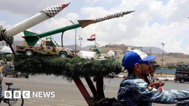 Houthi militiaman rides in front of sculpture of missiles