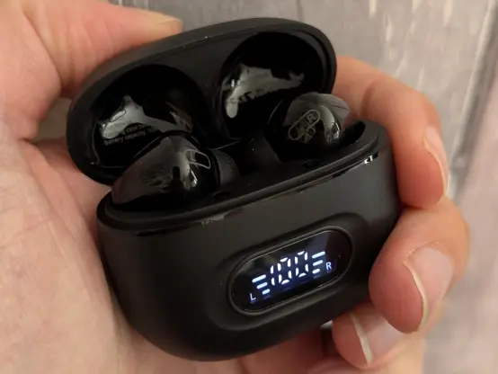 Black headphones in a black case. An LCD shows the charging level.