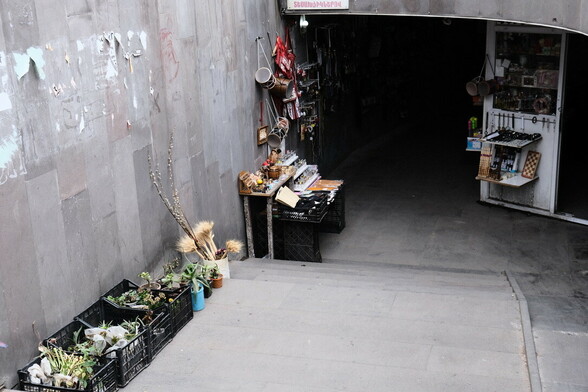 there are plastic boxes with goods to be sold in the entrance of the underground passage. there are home plants, dried flowers, pots, chess and other games among the goods