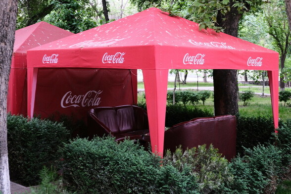 there are two sofas under a red coca cola tent among the trees in the park
