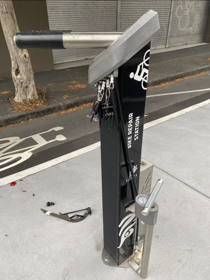 Close-up image of bike repair station on a Melbourne bike lane. It has a cool collection of a dozen or so tools on lanyards that you can pull down to your bike for repairs. It Lao has a pump. This is located opposite the Peel in Melbourne.
