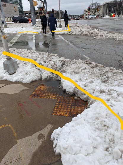 Photo of a sidewalk with snowy curb extensions several feet beyond it's boundaries. The location of the curb under the snow  is marked in yellow. 