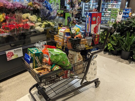 A shopping cart rather full of miscellaneous groceries. 