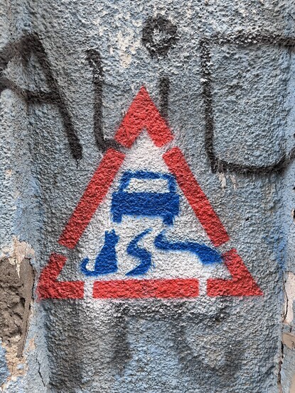 a graffiti which resembles a triangle traffic sign that marks slippery road ahead — but there is also a cat on the road
painted on a gray blue wall 