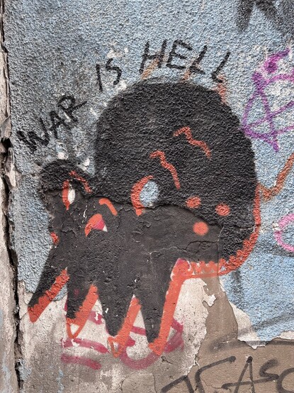 a graffiti with “war is hell” and a black stylised skull
painted on a gray blue wall 