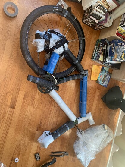 Disassembled bicycle lying on floor with foam padding taped around all tubes 