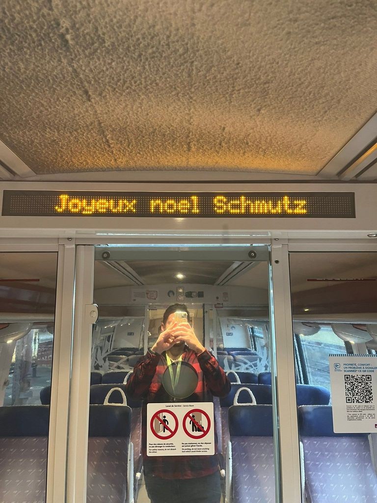 A train driver uses his phone to take a picture of the scrolling display above the door to a passenger coach, which reads "Joyeux noel Schmutz"