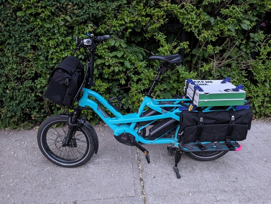 Pizza boxes mounted on the back of a Tern GSD cargo bike using adjustable quick clamps wedged between the cargo bags and the frame. 