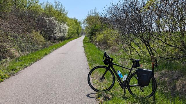 Dark brown Diverge bicycle leaning against milepost 13 looking East with blooming pear trees on the left of the Sakatah Singing Hills State Trail.