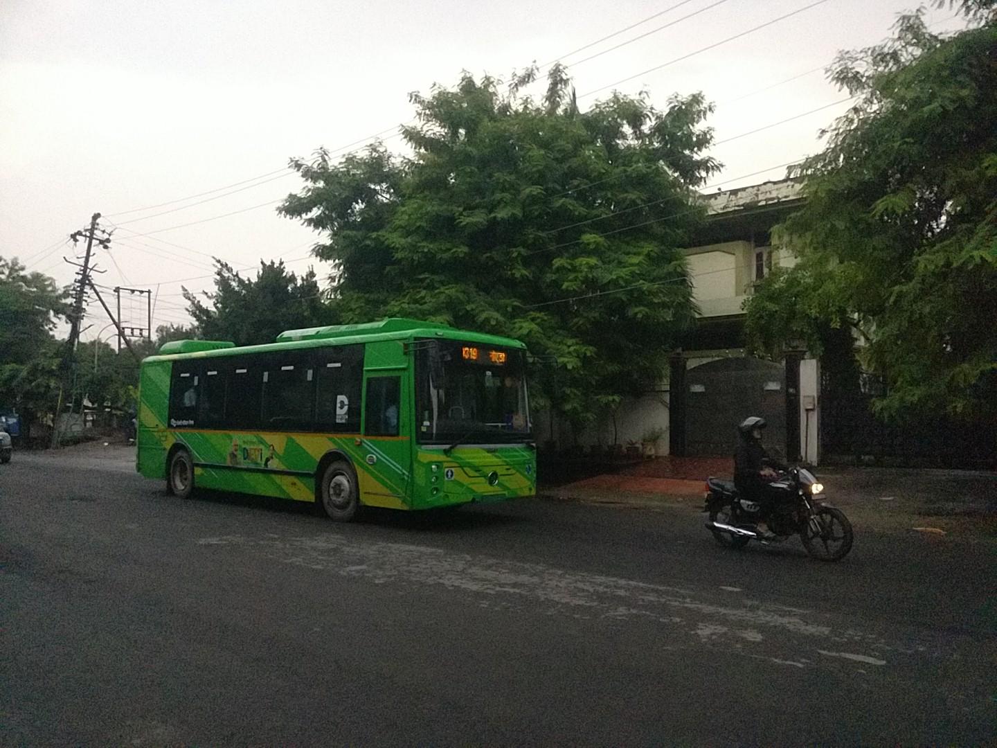 A 9 meter PMI Pegio bus in its flashy green livery behind a person on a bike contrasting the older city and street with its new design