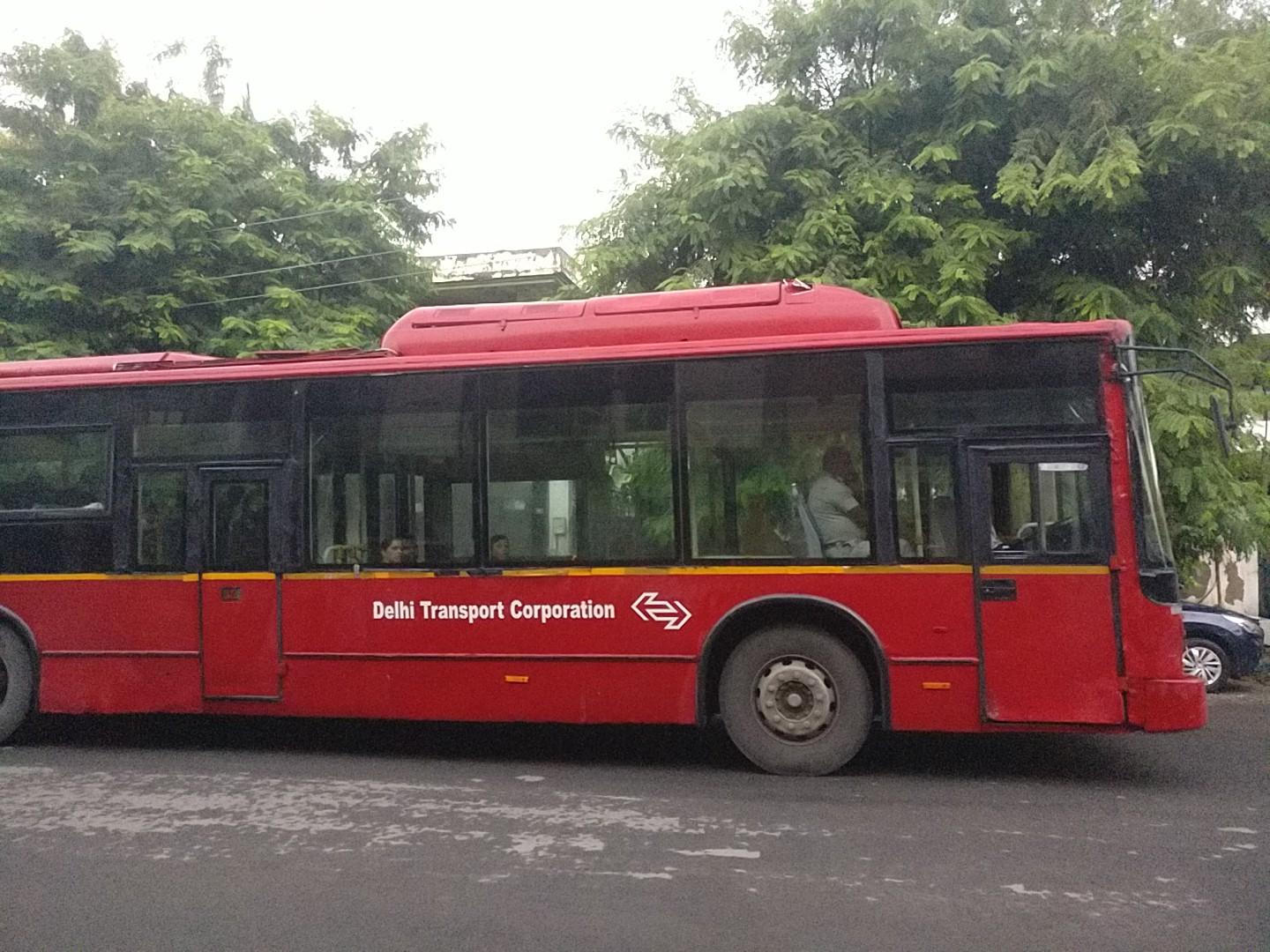 Airconditioned Ashok Leyland bus from the otherside with clean bold text marking it as part of the "Delhi Transport Corporation" followed by the logo in white atop the red bus,
