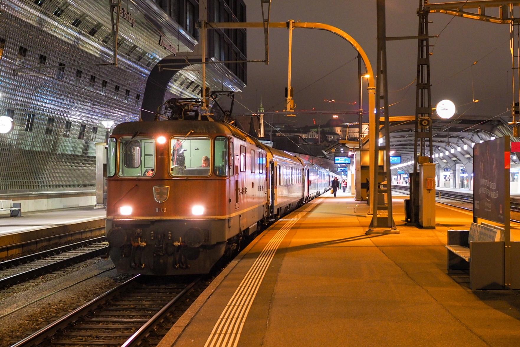 A class Re 4/4 II locomotive at the front of the train at Zurich HB at night.