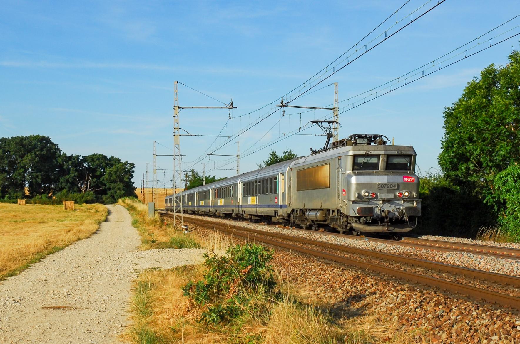 On a stretch of railway next to a dirt path through the fields, a fantôme liveried Nez Cassé with 7 Corail carriages on her way towards Paris.